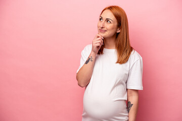 Young caucasian pregnant woman isolated on pink background looking sideways with doubtful and...