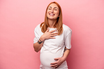 Young caucasian pregnant woman isolated on pink background laughs out loudly keeping hand on chest.