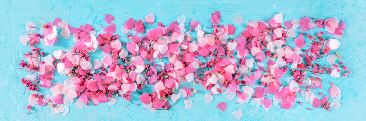 Valentine day panorama with pink hearts and flowers confetti, a flat lay panoramic banner on a blue background
