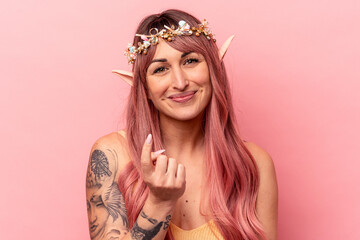 Young caucasian elf woman isolated on pink background pointing with finger at you as if inviting come closer.