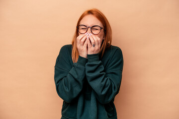 Young caucasian woman isolated on beige background laughing about something, covering mouth with hands.