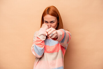 Young caucasian woman isolated on beige background throwing a punch, anger, fighting due to an argument, boxing.