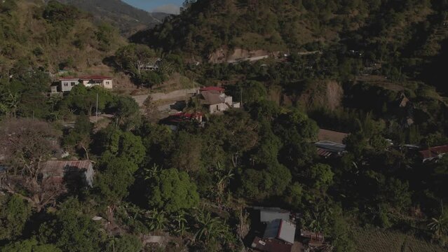 Aerial flying away from  an unfinished building house in a small mountain village in the middle of nature wilderness farms fields in Kabayan, Benguet, Philippines revealing the entire village
