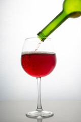 red wine from a bottle is poured into a glass on a light background. alcoholism and addiction. drinks for the holiday