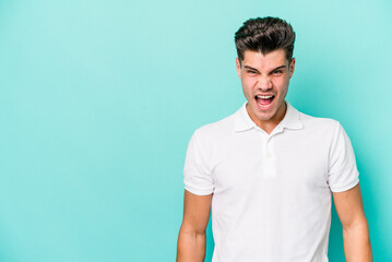 Young caucasian man isolated on blue background shouting very angry, rage concept, frustrated.