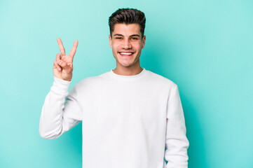 Young caucasian man isolated on blue background joyful and carefree showing a peace symbol with fingers.