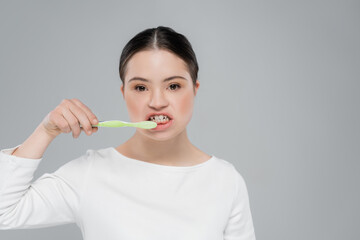 Woman with down syndrome brushing teeth isolated on grey © LIGHTFIELD STUDIOS