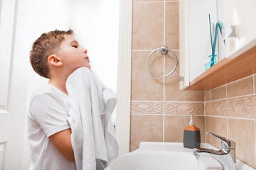 Health care, morning routine, wellness. Cute preteen boy wiping his face with a towel in the bathroom. © Iryna Dincer