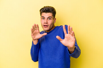 Young caucasian man isolated on yellow background being shocked due to an imminent danger