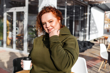 Portrait of a overweight smiling woman posing with a cup of coffee in her hand. Cafe at the background. Concept of psychology