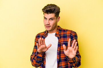 Young caucasian man isolated on yellow background rejecting someone showing a gesture of disgust.