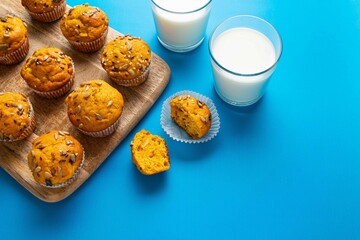 Pumpkin muffins with spices and seeds and milk on blue background. Copy space. Autumn, halloween, thanksgiving baking concept.