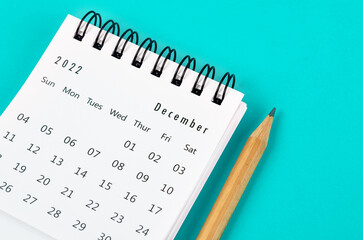 December 2022 desk calendar with wooden pencil on light blue background.