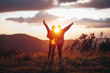 two happy girls with raised hands in the mountains at sunset