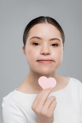 Young woman with down syndrome holding heart shaped sponge isolated on grey