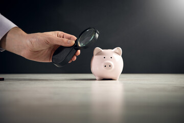 Man looking at piggy bank throught magnifying glass.