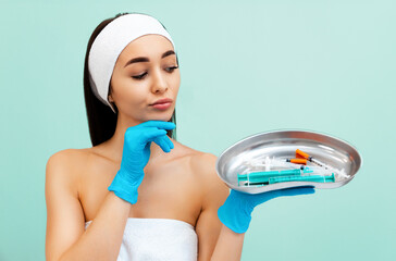 Portrait of a thoughtful young pretty woman in medical gloves choosing syringes from medical kidney...