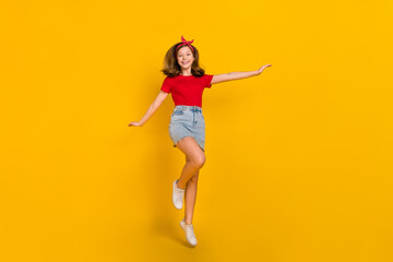 Fototapeta na wymiar Full size photo of cool teen girl jump wear red t-shirt hairband skirt shoes isolated on yellow color background
