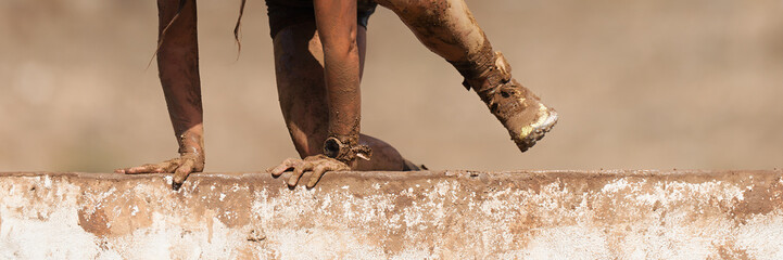 Mud race running. Running over obstacles female race participant, climbs over wall on obstacle...