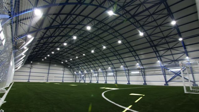 Modern empty indoor soccer field covered with green artificial grass and protective net in sports school gym