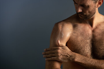 Close up of handsome masculine man applying cream or moisturizing body lotion onto body in...