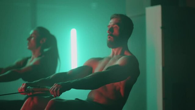 Slow motion: Man and woman training on a rowing machine in gym