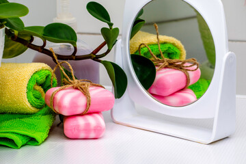 a stack of towels soap tied with string a houseplant and a mirror on the table in the bathroom