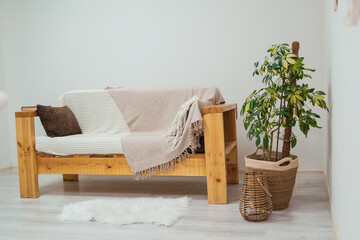 Fototapeta na wymiar Scandinavian style wooden sofa with plaid and pillows. Indoor plants in the interior.