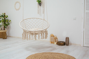 Wicker swing chair on ropes in a large bright room. Scandinavian style interior.