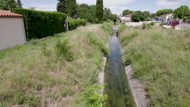 Water irrigation ditch near a residential area in Gignac France, Aerial tilt up reveal shot