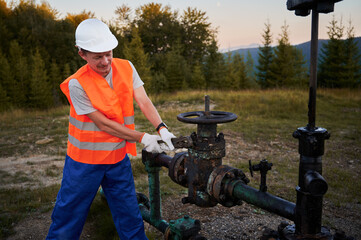 The gas production operator in protective helmet regulating gas pressure on oil pipeline outdoors....