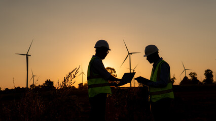 silhouette of engineer with laptop  on wind turbine on sunset.