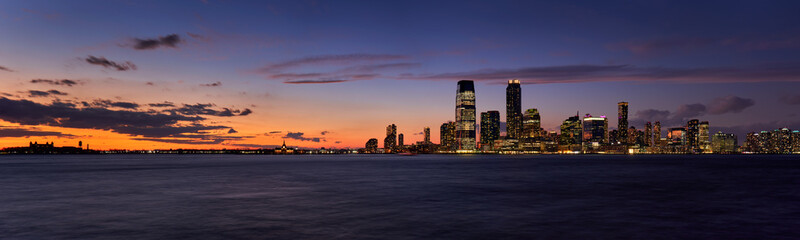 Fototapeta na wymiar Panoramic view of Downtown Jersey City skyscrapers after Sunset. Riverfront view of the Hudon River at twilight from Ellis Island to Exchange Place to Newport, New Jersey
