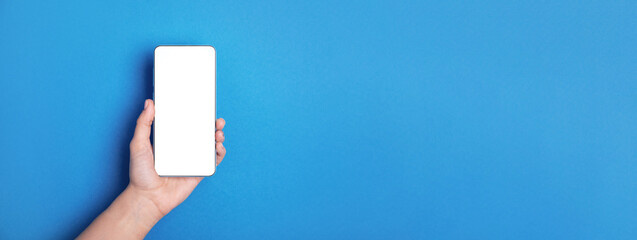 hand holding mobile phone with white blank empty screen over blue background, panoramic  layout