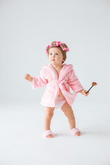 Cute little baby girl in pink terry with makeup isolated on a white background, repeats the behavior of mom