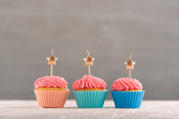 Festive cakes on wooden table. Muffins decorated pink buttercream and candles on gray background. Copy space