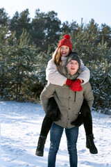 Happy loving couple is having fun in winter outdoors. Guy rolls girl on his back.