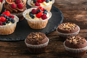 Chocolate muffins with nuts and vanilla muffins with mix of fresh berries on wooden table.