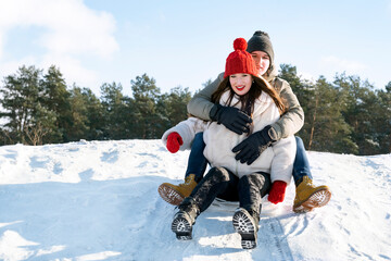 Young couple slide down the snow slide against the background of the forest and the blue sky. Winter sunny day