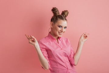 Young smiling girl in pink clothes with bun hairstyle on pink background. Pink mood.