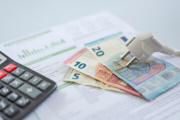 a white electric cap, euro banknotes, and a calculator on an electric bill, . Rising cost of...