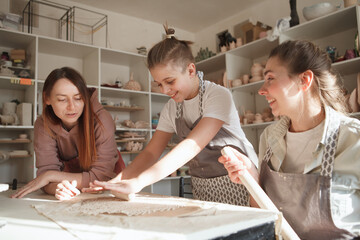 Professional ceramist teaching pottery to a young boy and his mom - obrazy, fototapety, plakaty