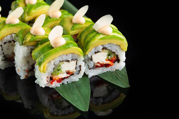 Traditional delicious fresh sushi roll set on a black background with reflection. Sushi roll with rice, nori, cream cheese, tobiko caviar, avocado. Sushi menu. Japanese kitchen. Asian restaurant.