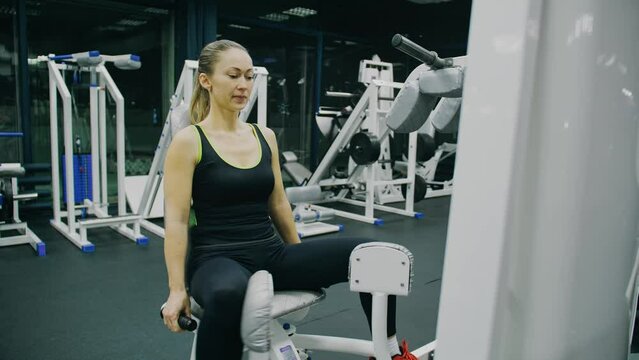 Fit Athletic Woman Girl Work out in Adduction Inner Thigh Machine, Doing Her Fitness Exercise. Muscular Women Training in Modern Gym. Sports People Workout in Adductor Exercising Fitness Center.