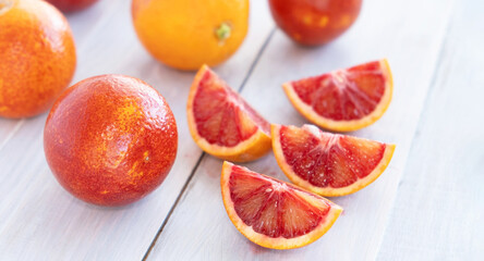Sliced quarters and whole ripe juicy Sicilian blood red oranges on wooden background. Selective...