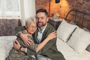 elderly pensioner mother embracing her middle-aged son and being grateful for his support. High...