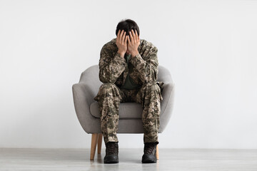 Unhappy man in camouflage sitting at arm chair, copy space