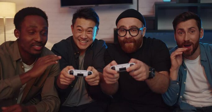 Portrait of Men Friends sitting at Home playing Video Games and Cheering. Happy Group of Diverse Male Students using PlayStation looking at TV sitting on couch. Night Party with Drinks. Goal. Winner