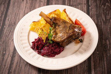 Food photography. Close up view of dish made of duck leg with potatoes aside against wooden background.