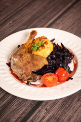 Food photography. Close up view of dish made of duck leg with potatoes aside against wooden background.